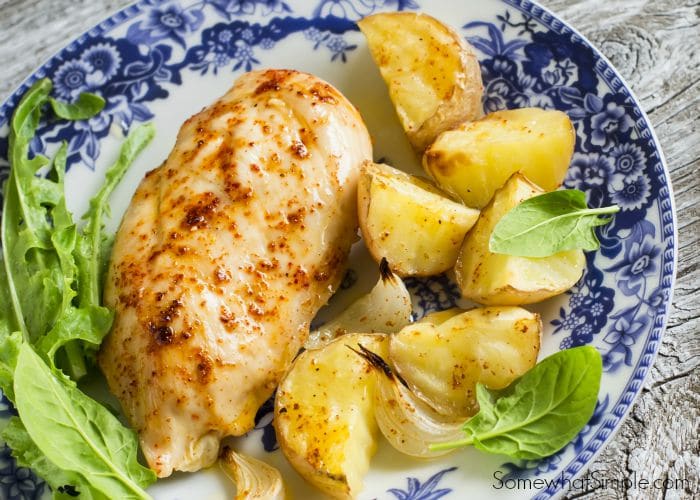 a piece of garlic chicken and a side of potatoes with pieces of garlic and greens as garnish on a plate that was made using this easy recipe
