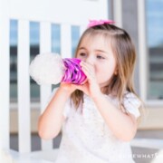 little girl blowing on a water bottle making bubble snakes