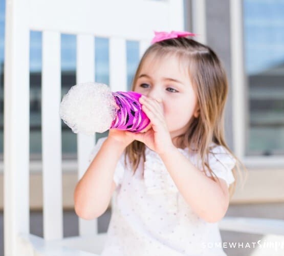 little girl blowing on a water bottle making bubble snakes