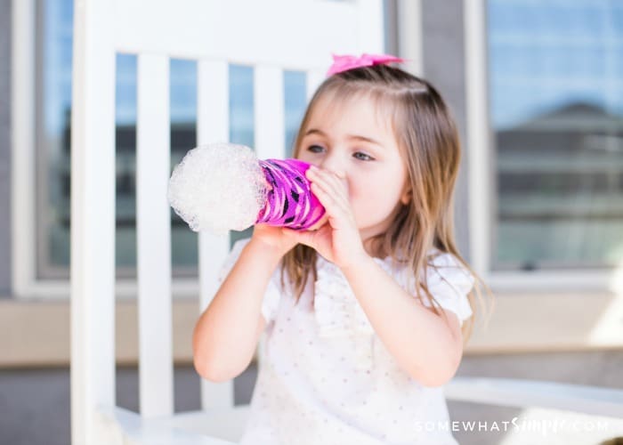 little girl blowing on a water bottle making bubble snakes