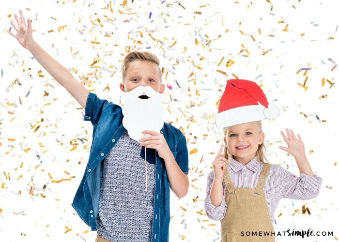 2 kids with holiday photo props standing under confetti