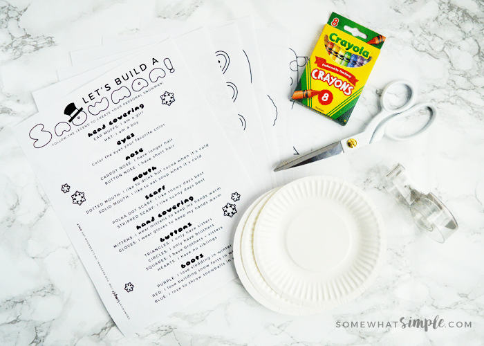 Build A Snowman Activity Kit with paper plates, scissors, tape and crayons on the counter
