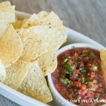 a small white bowl of fresh homemade mild salsa inside a larger white serving tray filled with tortilla chips.