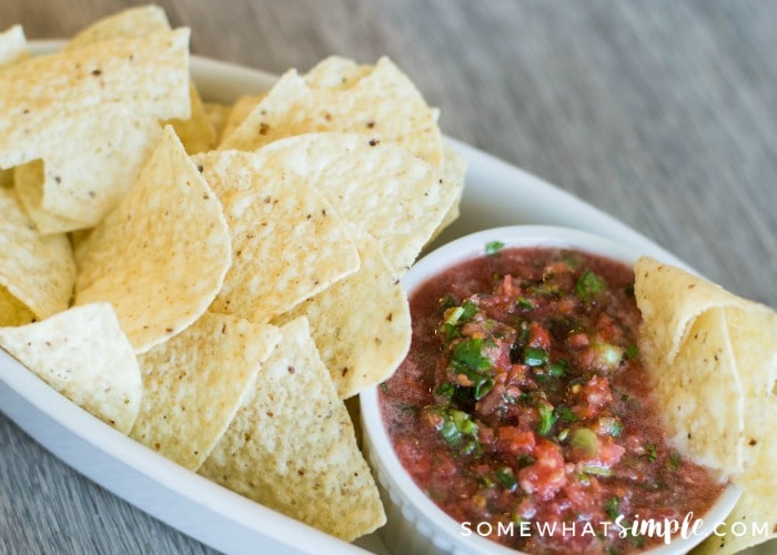 a small white bowl of fresh homemade mild salsa inside a larger white serving tray filled with tortilla chips.