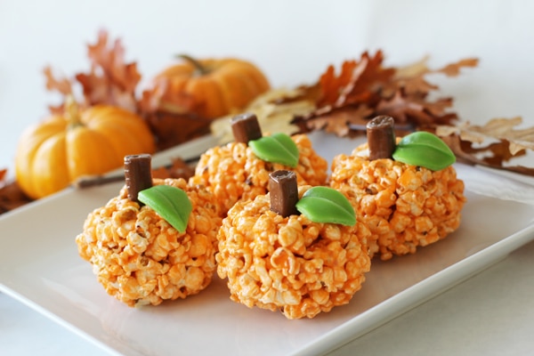 four Orange Halloween popcorn pumpkin balls on a white serving tray