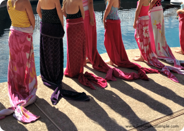 girls standing by a pool with mermaid tails made with beach towels