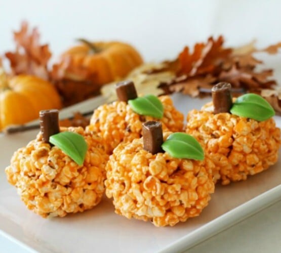 four Orange Halloween popcorn pumpkin balls on a white serving tray