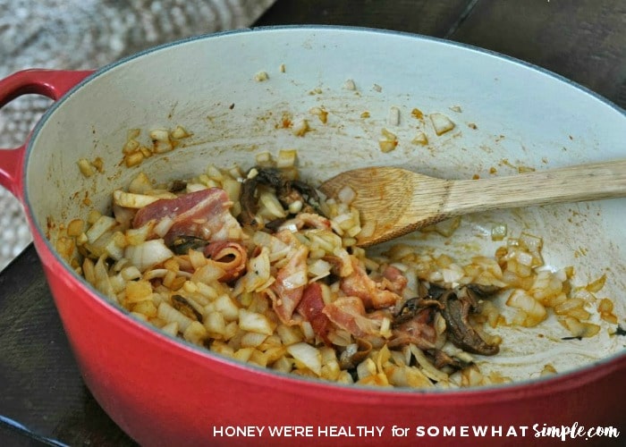 a red pot with onion, garlic, thyme, bacon, tomato sauce and porcini mushrooms being cooked on a stove top prior to being included in the lentil soup recipe