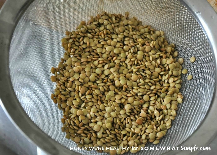 a strainer full of brown lentil beans that are being prepared for crock pot lentil soup