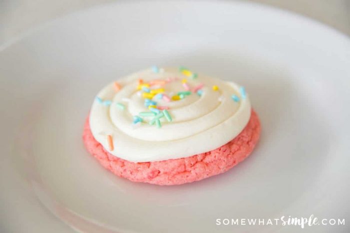 On Strawberry Cake Mix Cookie on a white plate with white frosting and colored sprinkles
