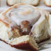 a forking cutting off the corner of a cinnamon roll with a cream cheese frosting on top