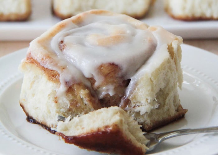 a forking cutting off the corner of a cinnamon roll with a cream cheese frosting on top