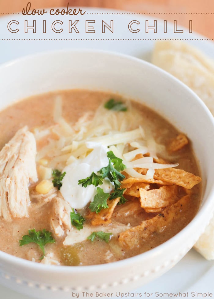 a close up of a white bowl filled with this crock pot White Chicken Chili recipe. The chili is topped with shredded cheese, cilantro, sour cream and tortilla strips. The words slow cooker chicken chili is written at the top of the image.