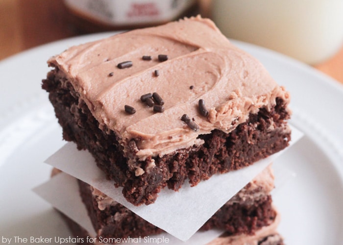 a stack of chocolate hazelnut brownies on a white plate with each brownie square being separated by a square of parchment paper.