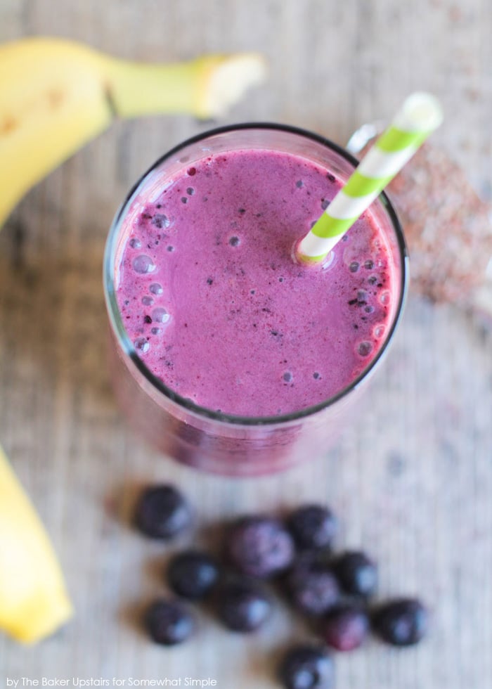 looking down on a glass of a blueberry pomegranate smoothie with a green and white straw