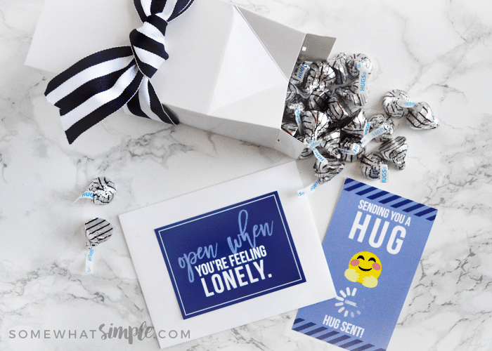 a dark blue card with a white envelope next to a white box laying on its side with Hershey's hugs spilling from the top