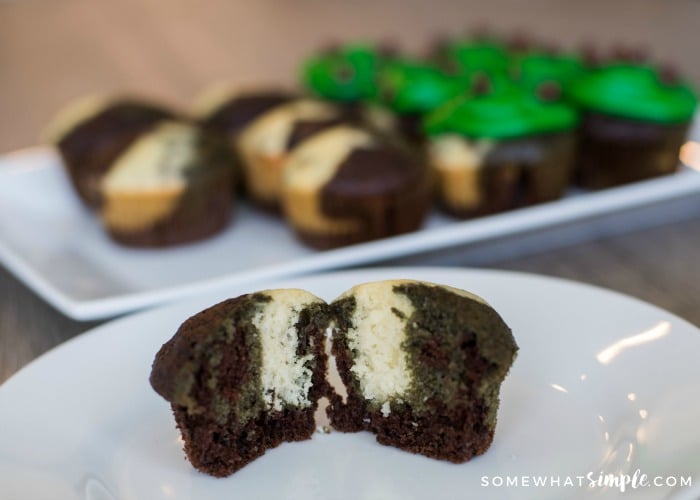 a camo cupcake that is green and shite cut open on a white plate with a tray of army cupcakes in the background