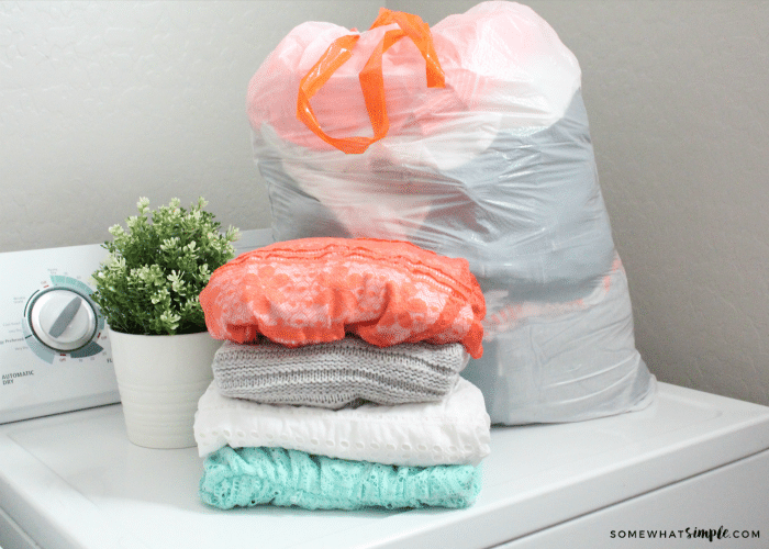 a stack of clothes and a trash bag full of old clothes sitting on a dryer