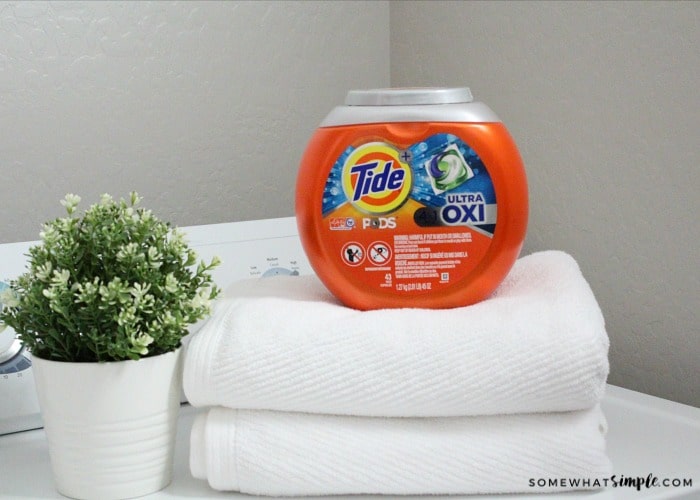 a small stack of white towels on top of a dryer with a container of Tide pods on top