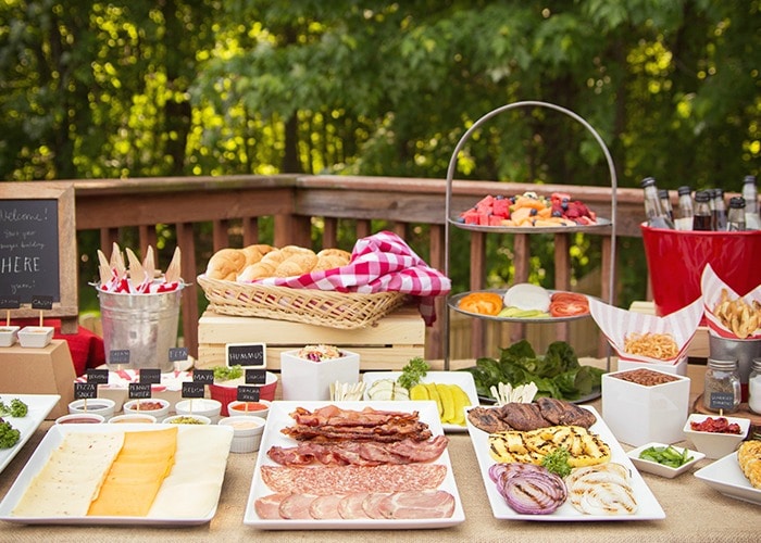 hamburger bar with trays of cheese, meats and vegetables on a picnic table make a perfect setting for a summer bbq