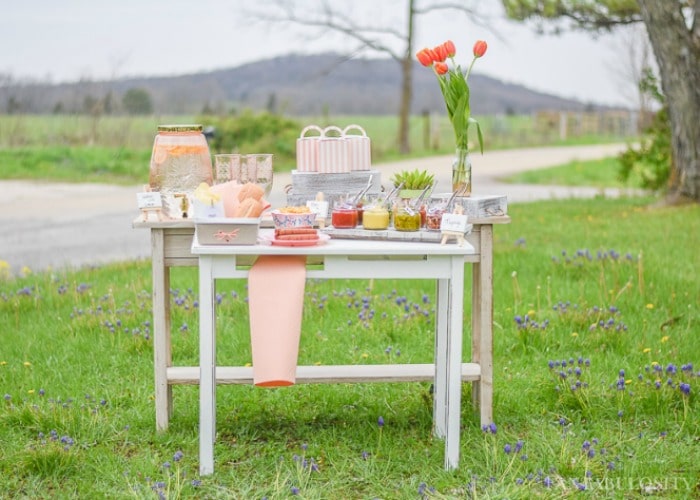 hot dog bar set out on white wood tables on the grass is a fun compliment to a summer bbq