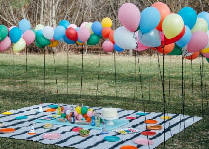 balloons on poles in a park with a picnic blanket on the ground