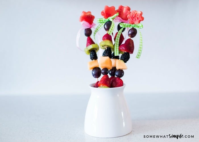 a tall white dish filled with fruit kabobs made with watermelon, grapes, strawberries and other delicious fruit