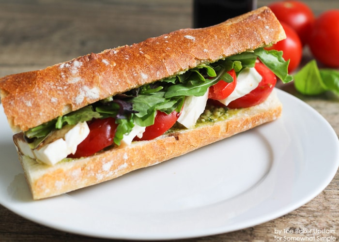 a Caprese Sandwich on a white plate filled with lettuce, tomatoes, mozzarella cheese and pesto made using this easy Recipe