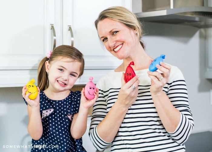 an attractive mother and standing next to her young daughter and each of them are holding a wacky sack in each hand. 