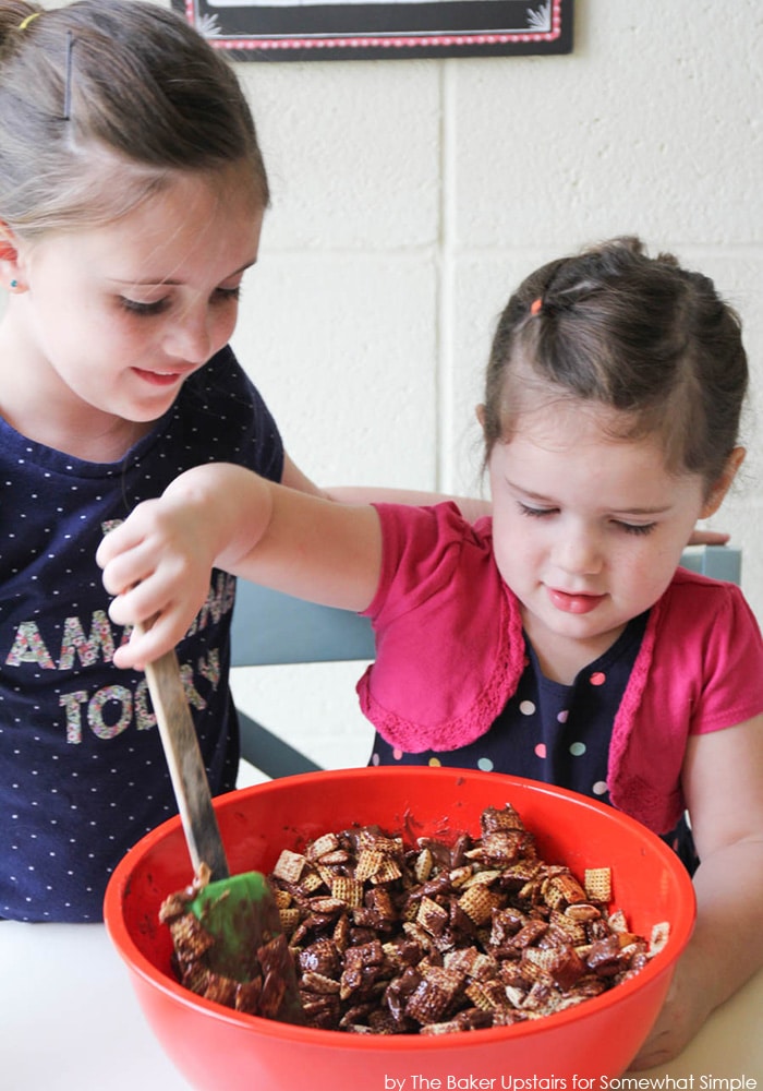 a little girl stirring a big bowl of ingredients used to make this Chex Muddy Buddies recipe