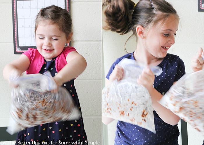 two girls shaking a plastic bag of chex mix muddy buddies