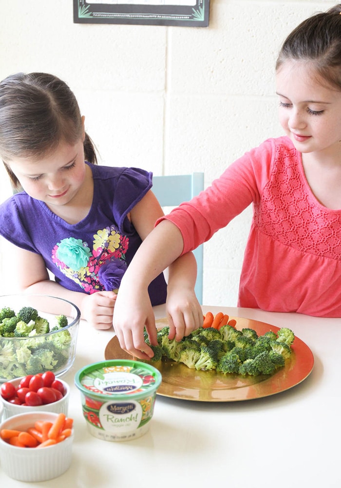 two girls arranging a vegetable tray in the shape of a Christmas tree