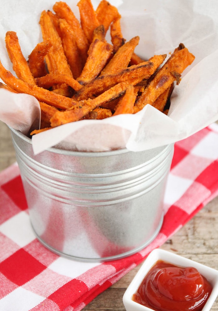 a close up of a metal serving bowl of crispy Sweet Potato Fries on a red checkered napkin and a side of ketchup