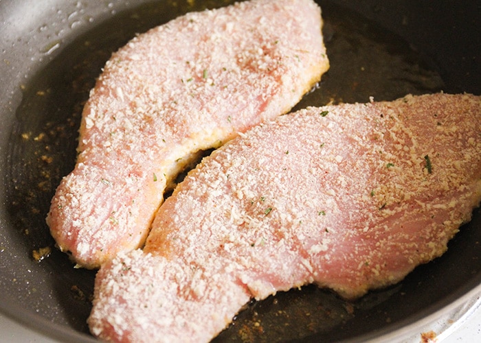 Turkey Cutlets covered in a garlic and Parmesan rub in a frying pan beginning to cook 
