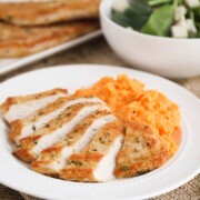 sliced Turkey Cutlets with a side of mashed potatoes on a white plate with a bowl of salad in the background