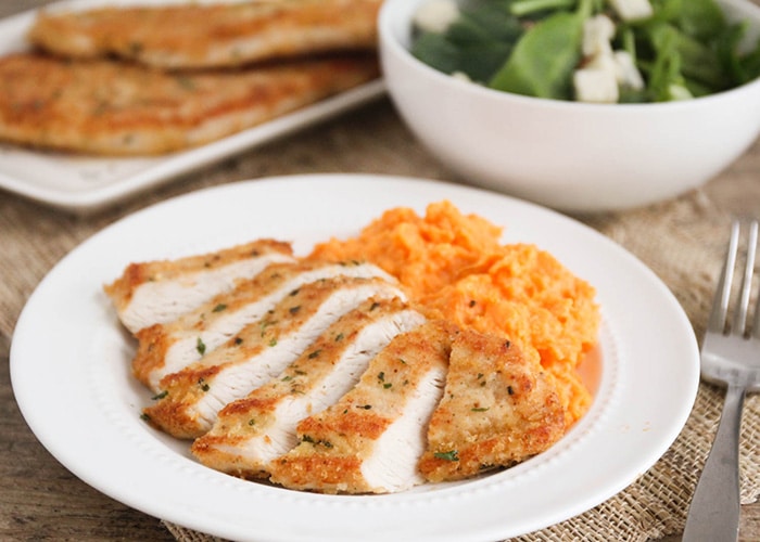 sliced Turkey Cutlets with a side of mashed potatoes on a white plate with a bowl of salad in the background