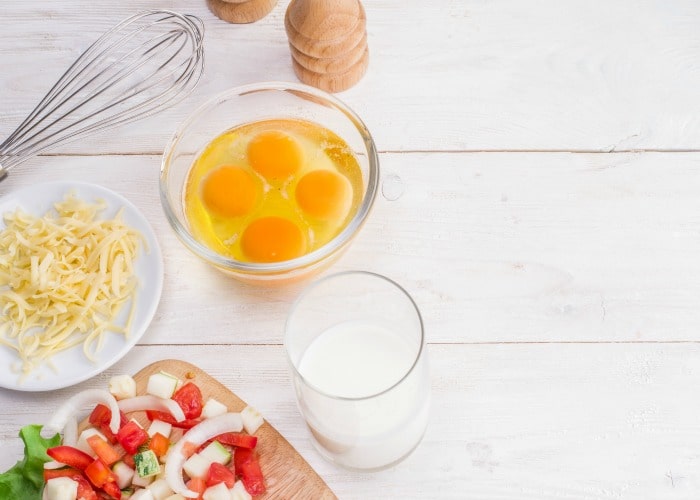 a bowl with four egg yolks, milk, cheese and chopped vegetables are the ingredients for an omelet to make while camping.