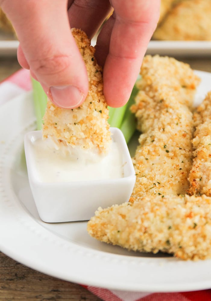 a hand dipping a piece of crispy chicken into a small dish full of Ranch dressing