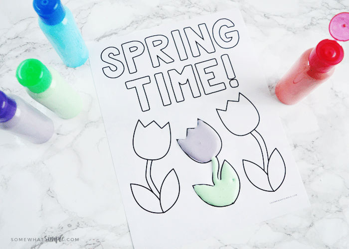 looking down on a coloring page that says "spring time" with one tulip painted with homemade puffy paint and bottles of green, purple, blue and red puffy paint next to the coloring sheet