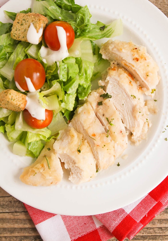 a piece of baked italian chicken made with italian dressing on a white plate with a garden salad on the side