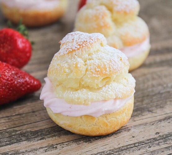 close up of a cream puff next to a strawberry