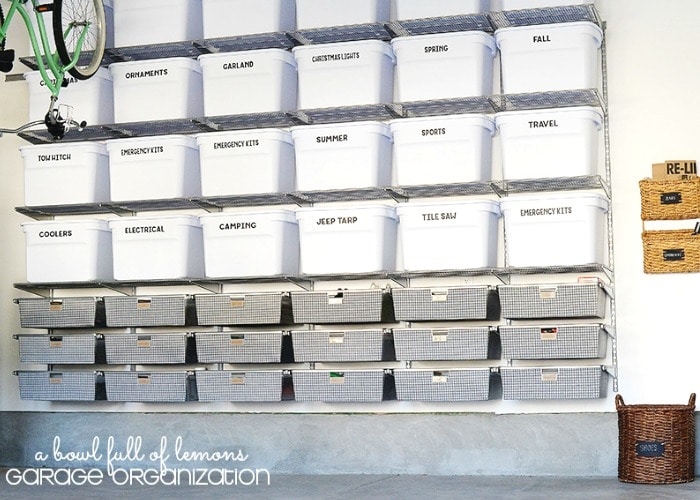a garage organized with several white bins stacked up with each having a label noting what's inside.