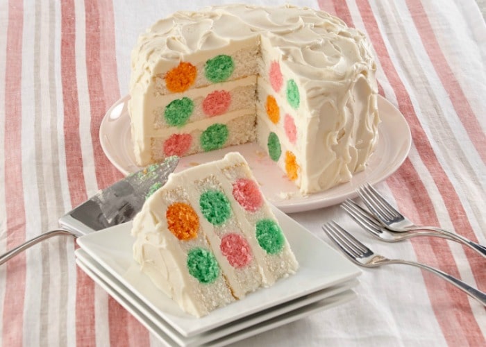 a layered vanilla cake with orange green pink and yellow polka dots with white frosting.