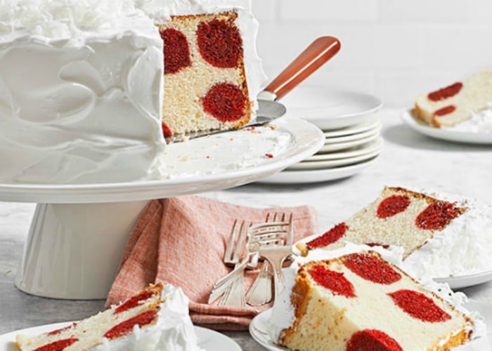 a vanilla cake with white frosting that has a few pieces cut out and are sitting on plates. The cake and the slices all have large red polka dots