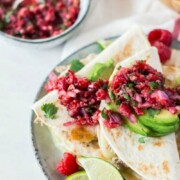 a plate piled high with slices of quesadillas topped with a raspberry salsa and slices of avocado