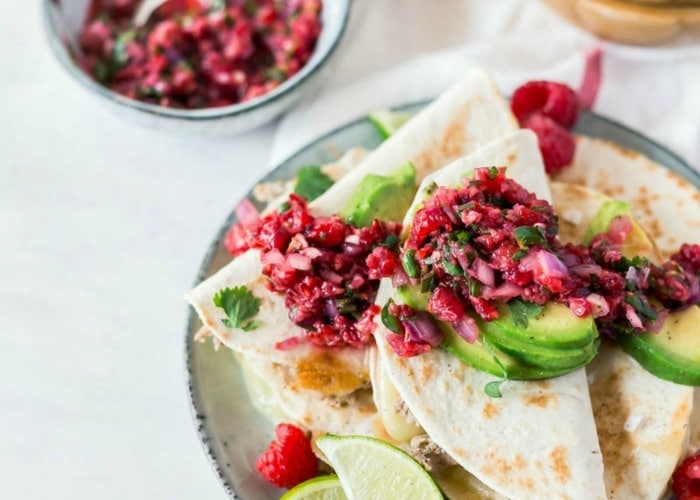 a plate piled high with slices of quesadillas topped with a raspberry salsa and slices of avocado