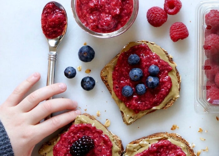 looking down on slices of toast topped with peanut butter, raspberry jam and blueberries