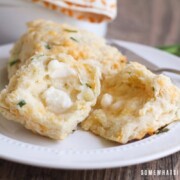 two cheddar biscuits with chives on a plate. One is cut in half with a pad of melted butter on top.