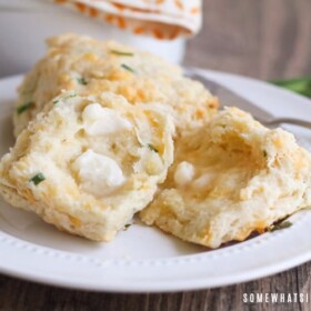 two cheddar biscuits with chives on a plate. One is cut in half with a pad of melted butter on top.