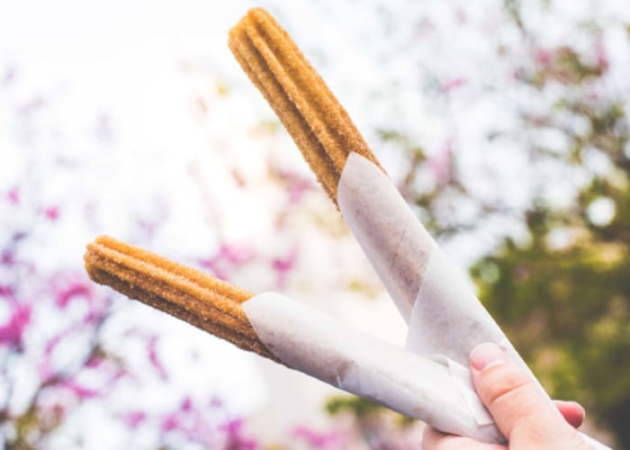 a hand holding two churros wrapped in paper